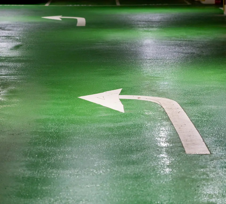 Green traffic coating with broadcast anti-slip aggregate, wet and catching the light, with a white arrow (stock photo)