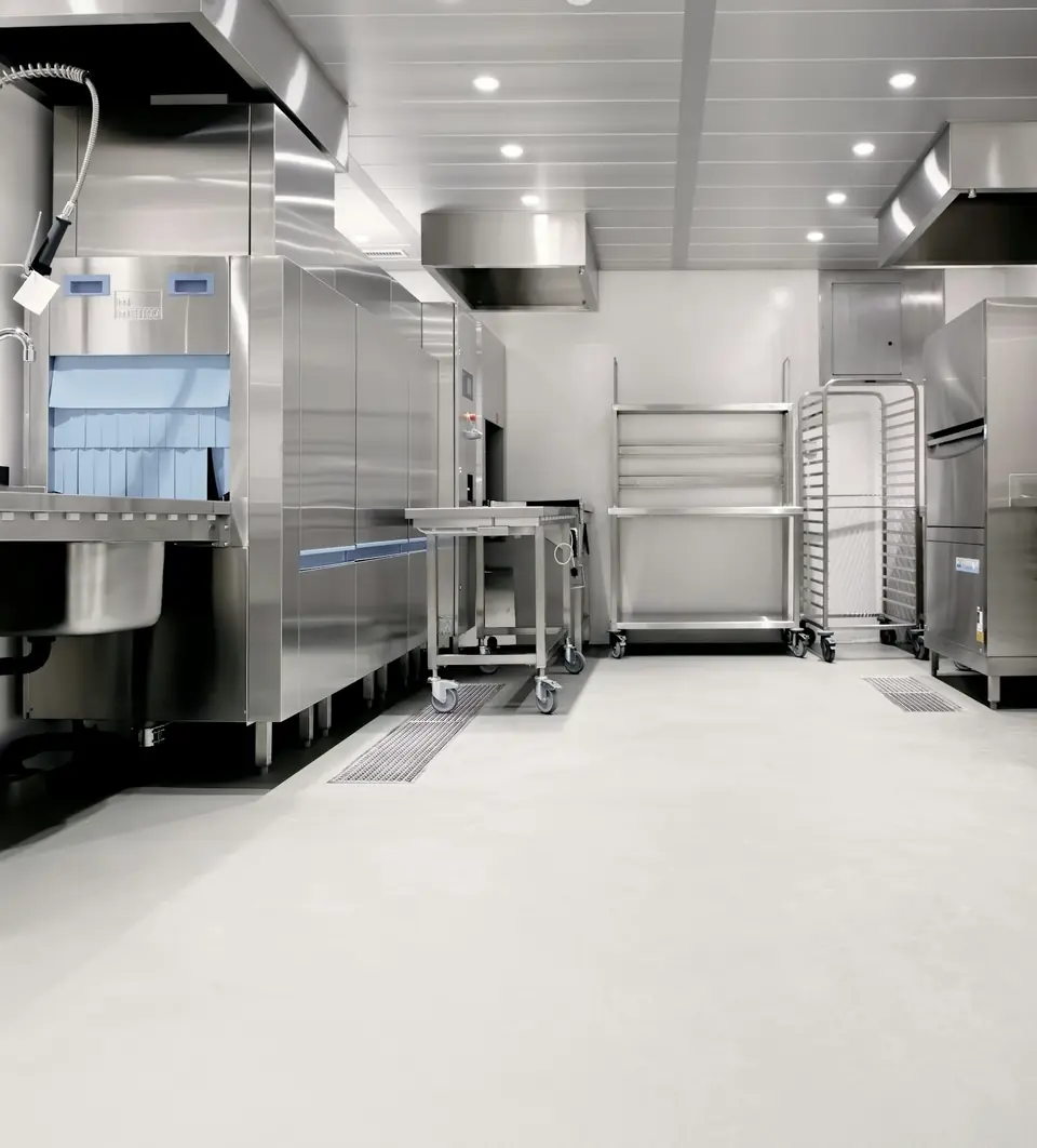 Commercial dish room with a seamless light-gray resin floor running to trench drains (stock photo)