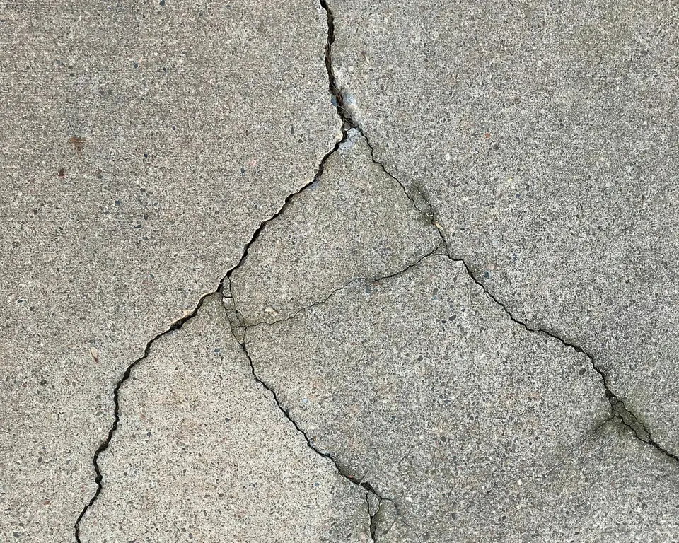 Broom-finished concrete slab with branching cracks that need repair before coating (stock photo)