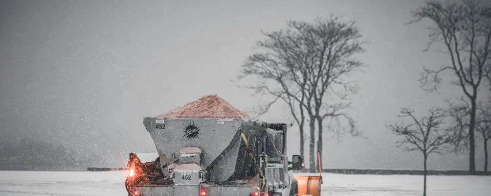Plow truck spreading road salt during a snowstorm, the brine that ends up on garage floors (stock photo)