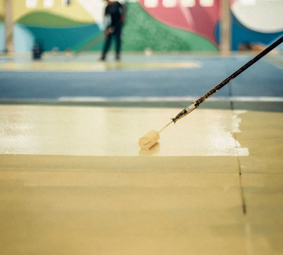 Long-handled roller laying down a fresh floor coating, the way a polyaspartic topcoat is rolled (stock photo)