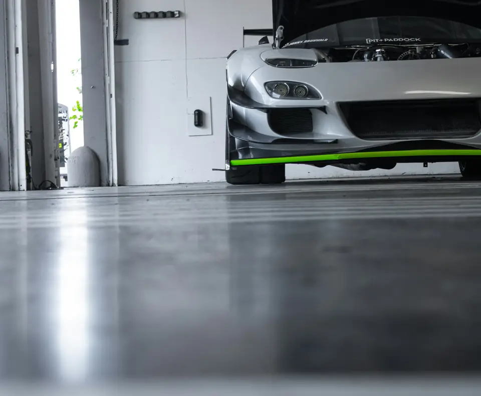Low view across a sealed gray concrete garage floor with a soft sheen toward a parked sports car (stock photo)