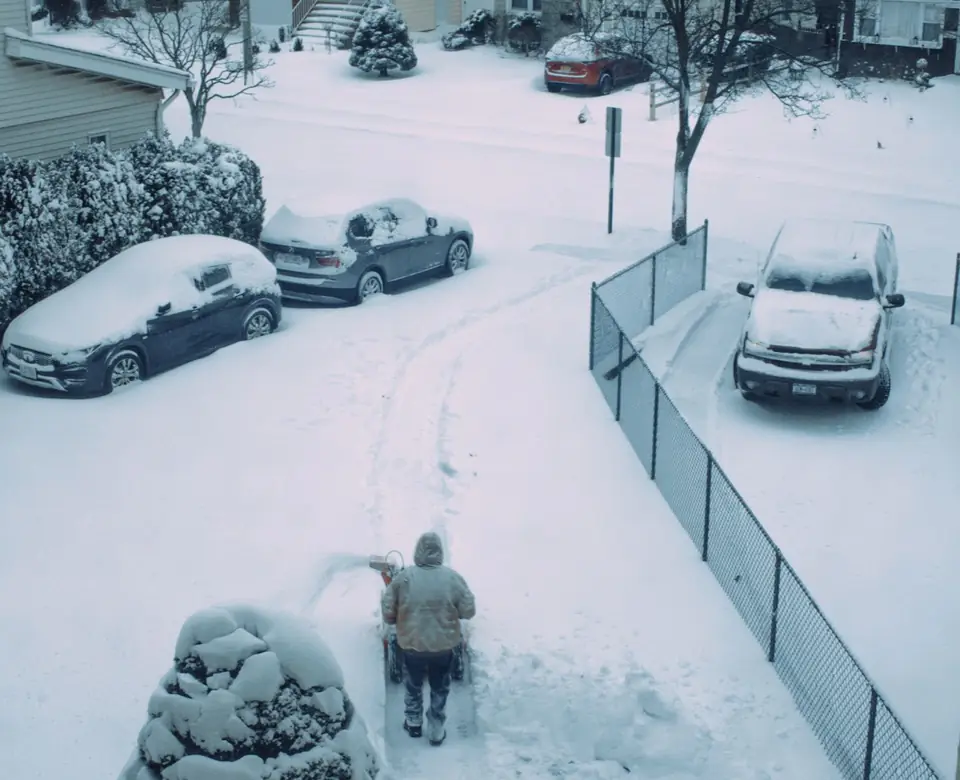 Homeowner clearing a suburban driveway with a snowblower in front of the garage (stock photo)