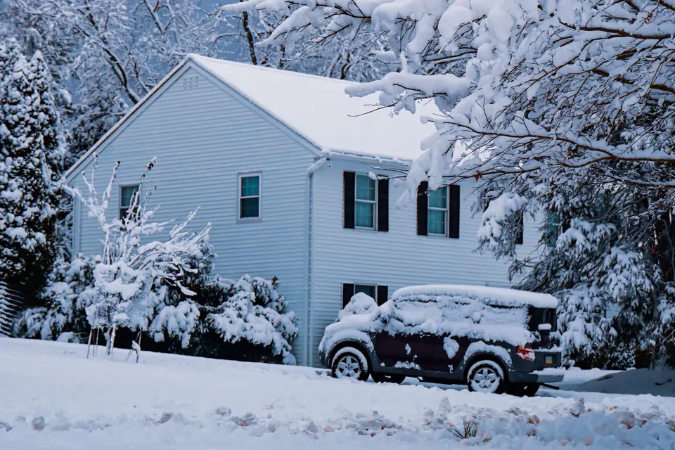 Snow-covered car parked in a suburban driveway, waiting to get back into the garage (stock photo)